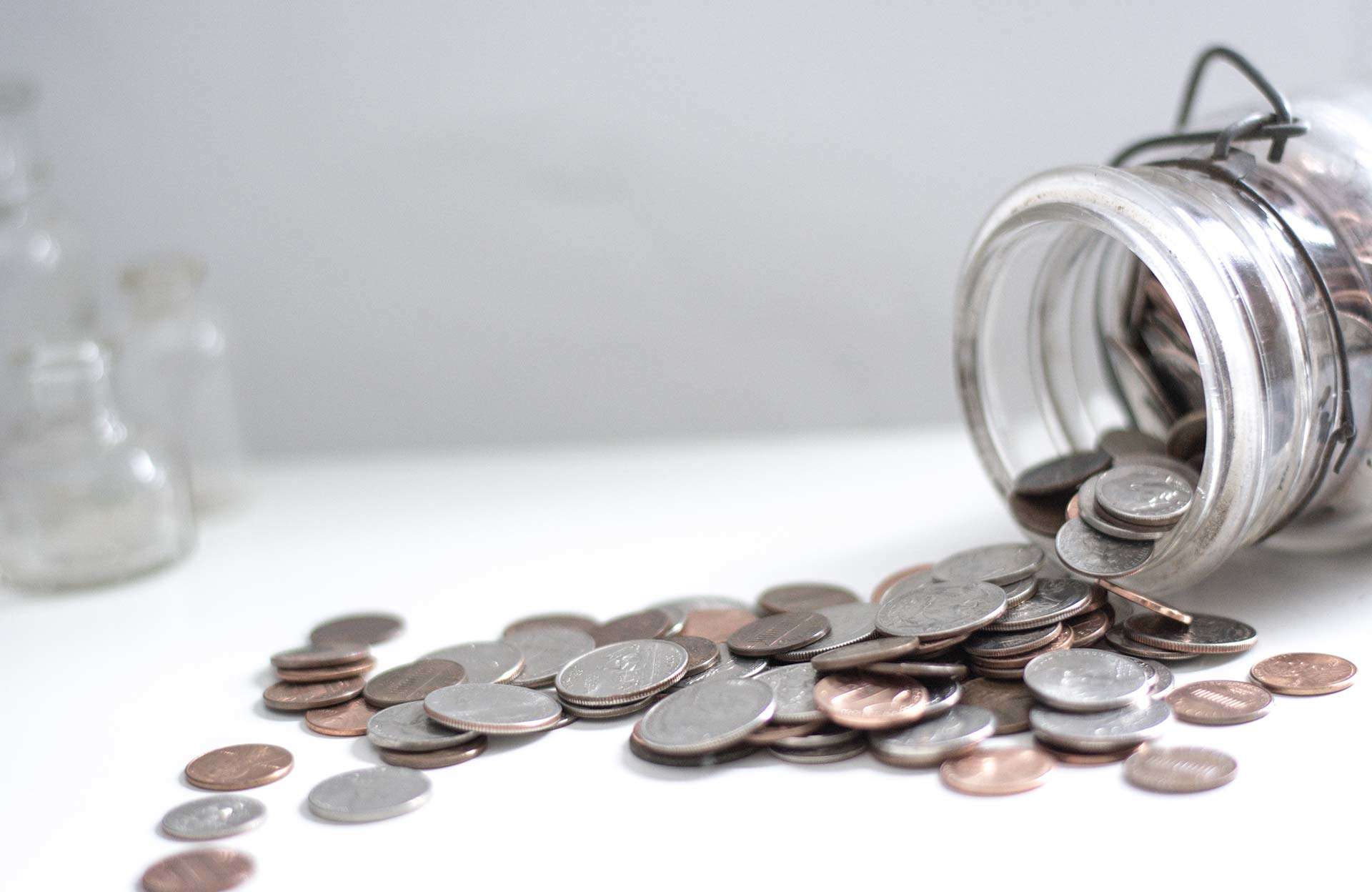 A glass cup with coins spilling out of it.