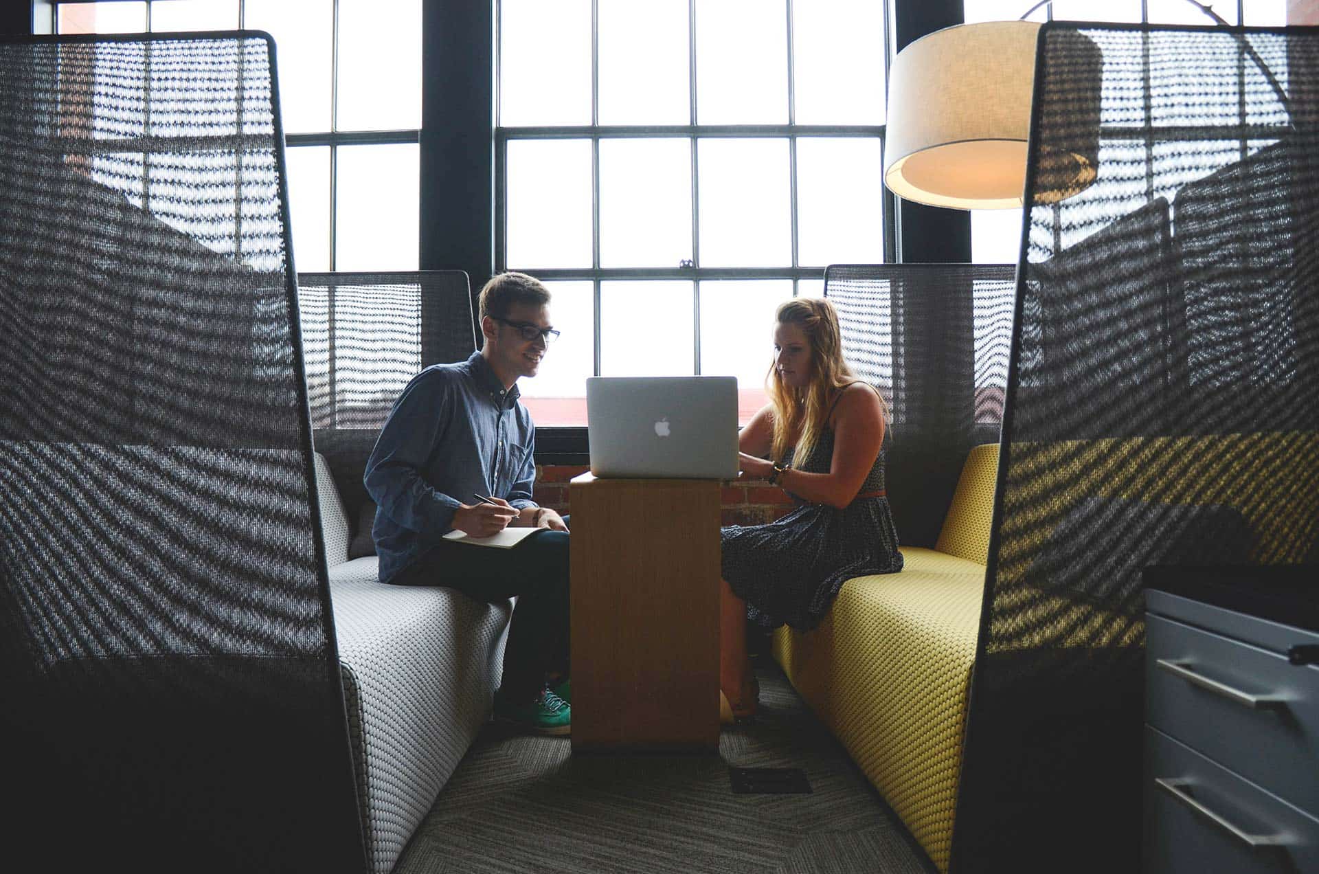 Two people sitting on a couch looking at a laptop.